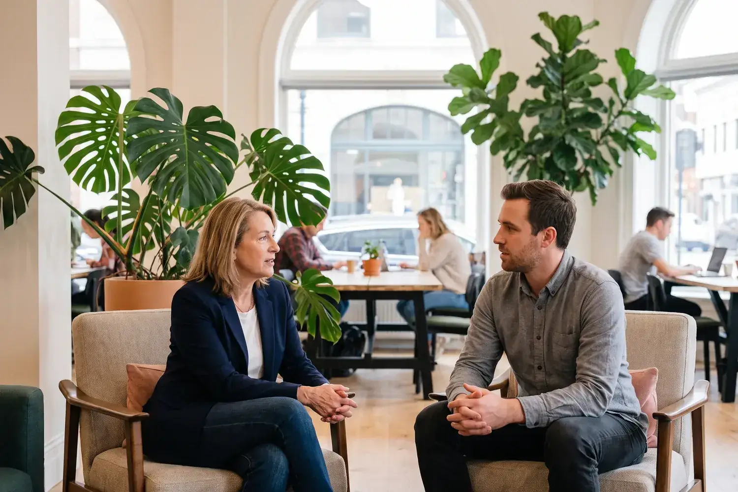 An executive and a founder talk one-to-one in armchairs in a plant-filled co-working space